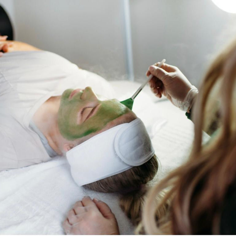 Person receiving a facial treatment with a green mask in a spa setting.